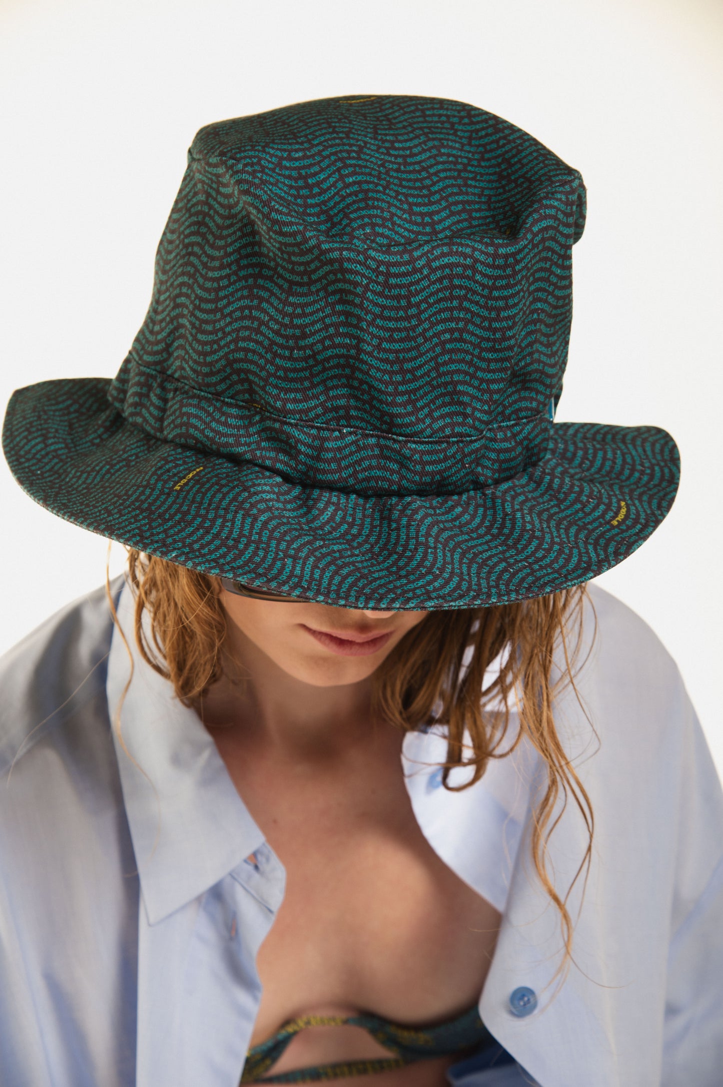 girl with Eero blue and grey oversized luxury hat printed with original lettering print with"the sea is a way of life" by Noodle Beachwear, with Terrence premium cotton shirt, Duffy Bikini and green soundglasses.