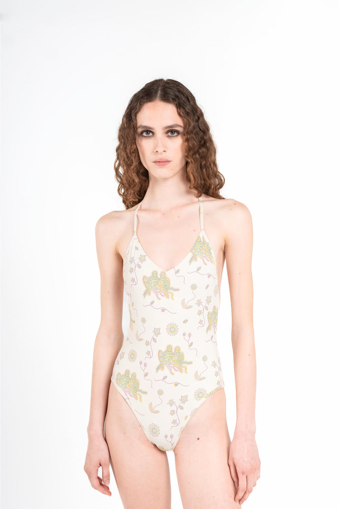 donna indossa costume intero jill di colore latte bianco con stampa a mosaico di pappagalli verdi gialli e viola con sole e fiori onirici dalla collezione nuova 2025 noodle mirage estiva di Noodle Beachwear

woman wears Jill one-piece swimsuit in milk white with mosaic print of green yellow and purple parrots with dreamlike sun and flowers from the new 2025 noodle mirage summer collection by Noodle Beachwear