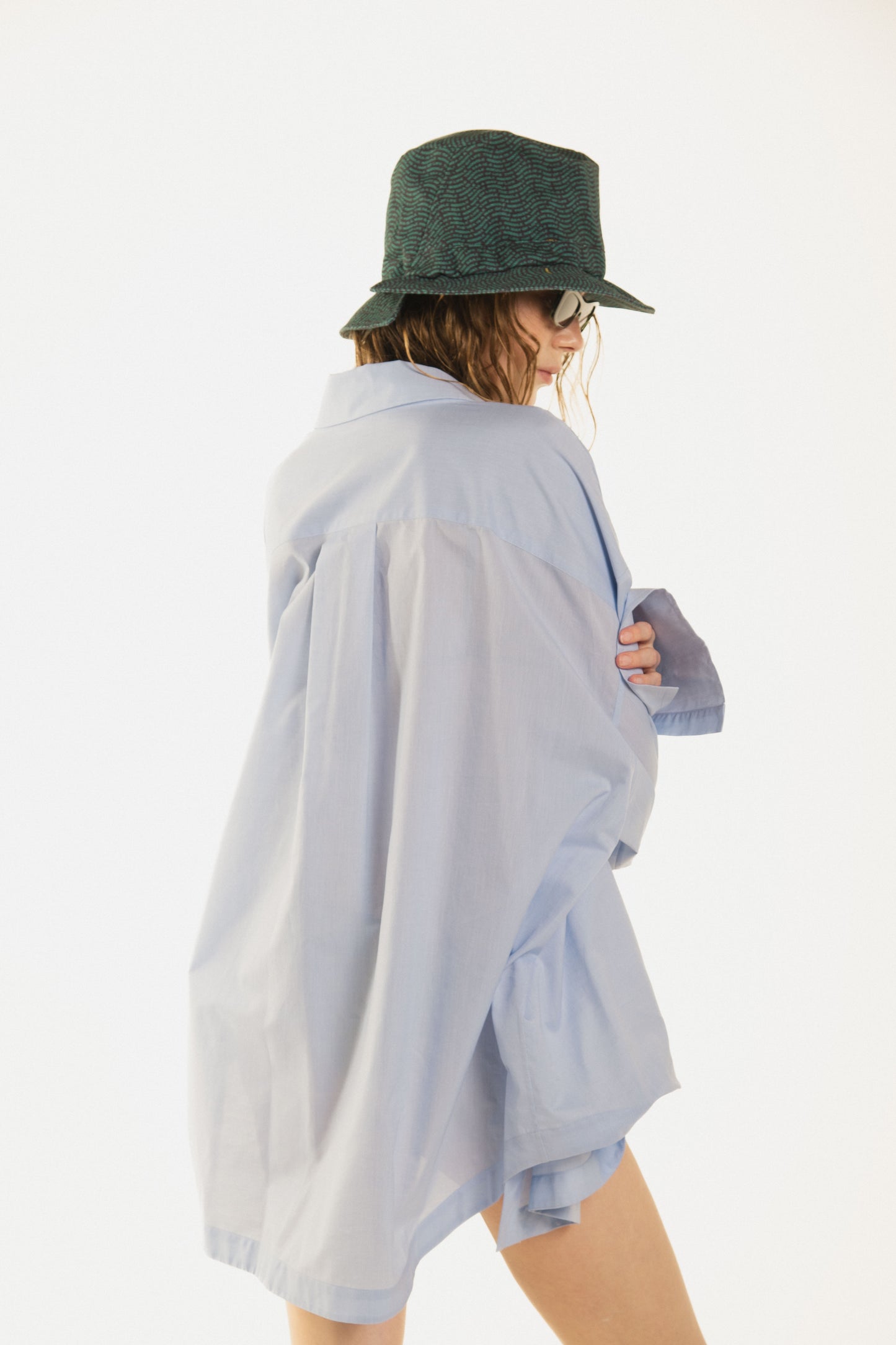 back view of girl with a beautiful blue waving shirt called Terrence  premium cotton and a curved button line, oversized fit. The model has Eero hat on her head