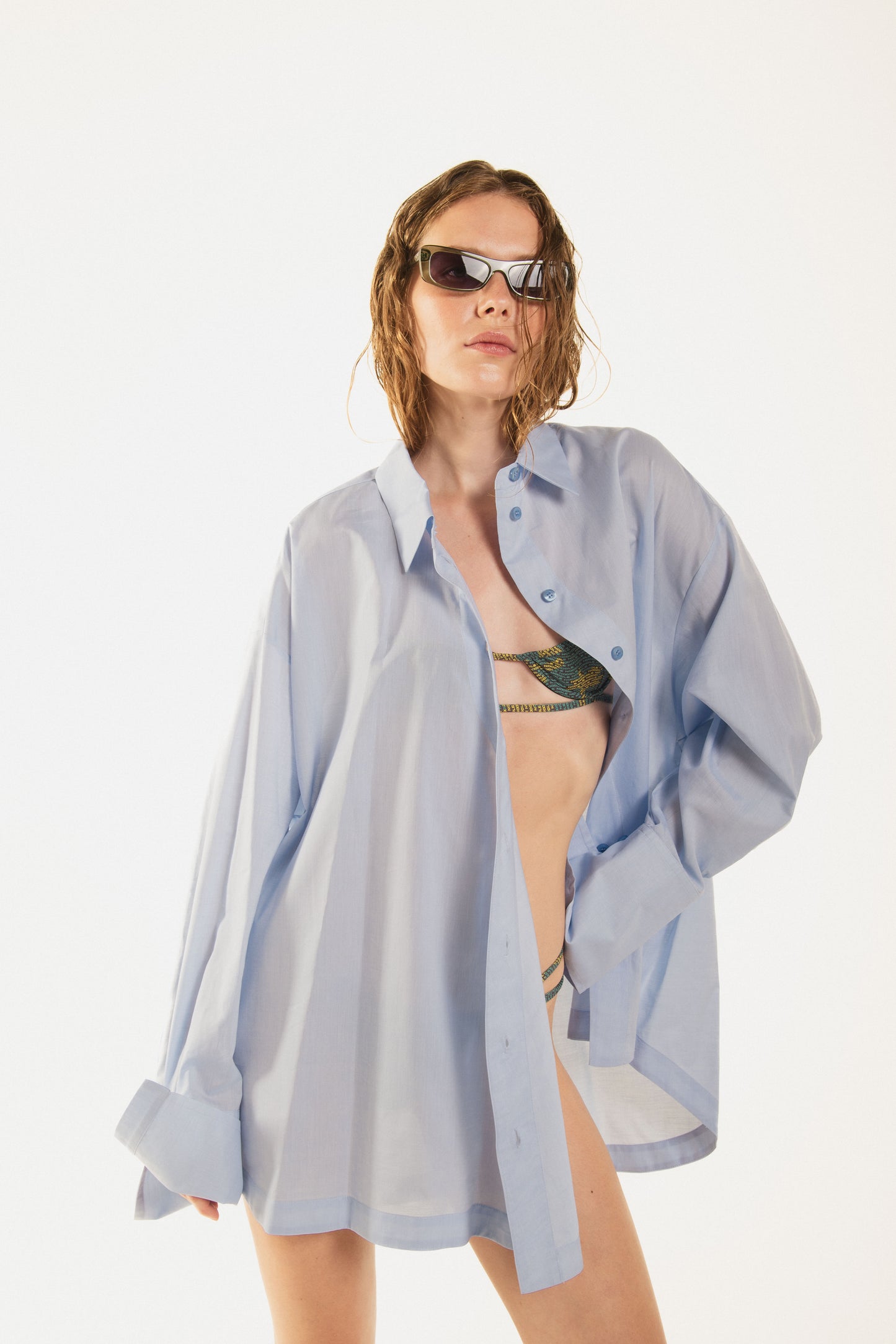 girl in a pose with a printed balconette bikini called duffy and Terrence waving shirt with premium blue cotton and a curved button line, oversized fit