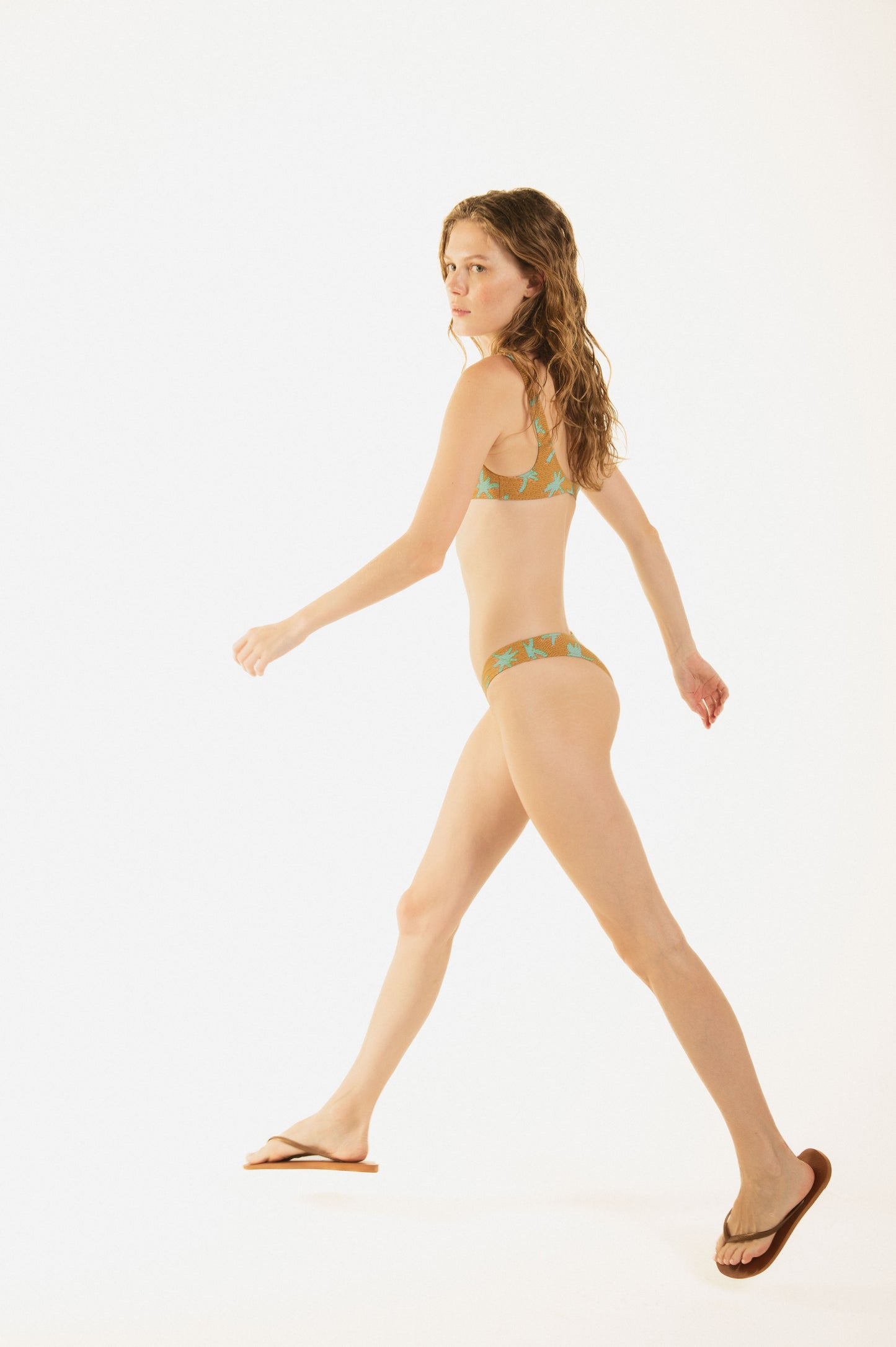 
                  
                    Side walk of a girl wearing Side view of girl wearing Zoe bralette printed brown bikini by Noodle Beachwear with reamy palms, with original noodle printed lining; best fabrics, perfect fit; kyoto palm sand variant
                  
                